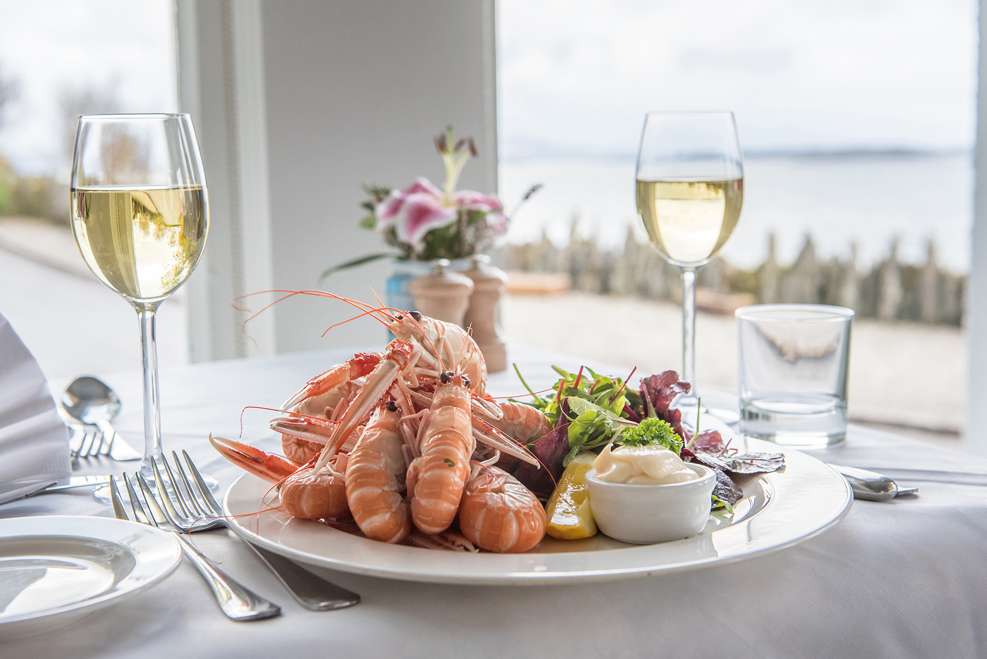 Plate of langoustines and glasses of white wine served at Crinan Hotel.
