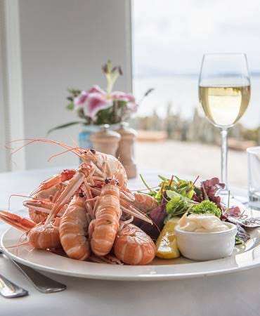 Plate of langoustines and glasses of white wine served at Crinan Hotel.