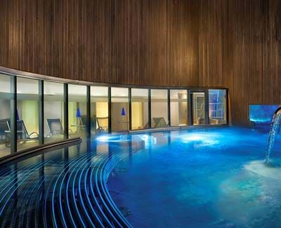 Modern spa hydro pool with curved design and waterfall feature, glowing in blue light.