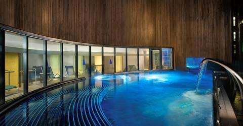 Modern spa hydro pool with curved design and waterfall feature, glowing in blue light.