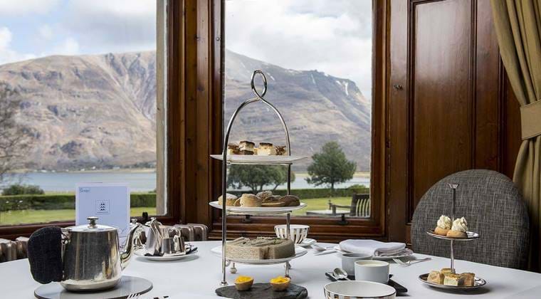 Afternoon tea set at The Torridon by a large window with a mountain and loch view in the background.