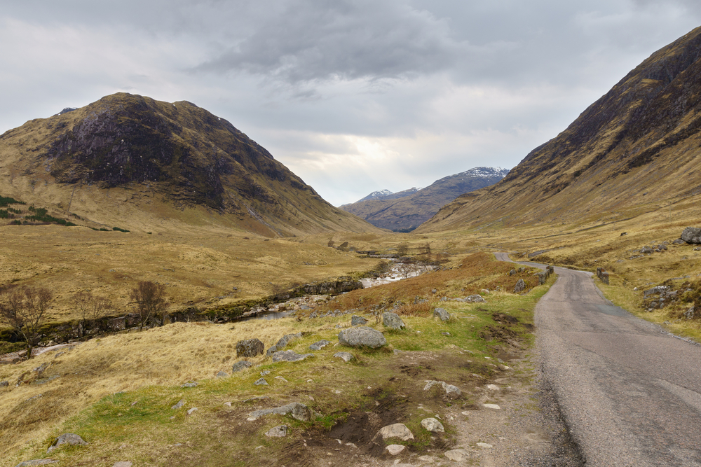 A rocky path through a valley with mountains in Perthshire looming in the distance, under dramatic skies.