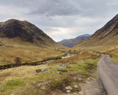A rocky path through a valley with mountains in Perthshire looming in the distance, under dramatic skies.