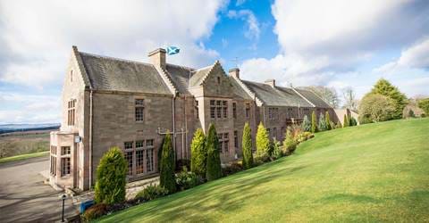 The Scottish stone house of the Murrayshall Hotel with a flag flying, nestled within a manicured lawn.