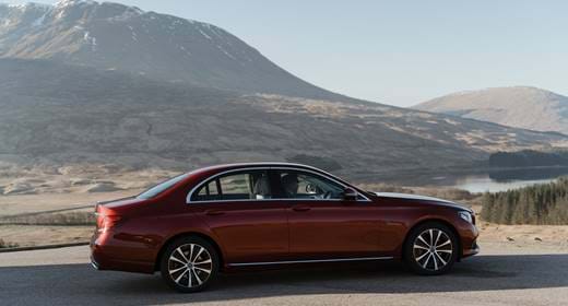 A red Mercedes-Benz sedan parked on a road with scenic mountainous landscapes in the background.